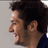 Pixelated close-up of a person's profile with dark curly hair, visible ear, and partial shoulder in blue clothing against light gray background.