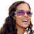 Pixelated close-up of a person with long dark hair wearing purple-tinted sunglasses and a checkered garment, mouth open in a smile.