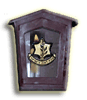 Dark purple arched frame with beige border contains shield emblem with book and plant, banner text, and candle-like element.