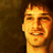 Pixelated close-up of a smiling person with light brown hair against dark background, rendered in warm orange and yellow tones.
