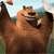 Brown cartoon bear with light brown chest and face, raised right arm holding a small red object, dark brown eyes and nose, open mouth showing teeth, standing against a blurred background of green and blue.