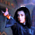 A person in a dark hooded garment with long hair, making hand gestures against blurred backgrounds.
