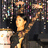 Pixelated static image of a figure with dark hair holding an object, set against a multicolored pixel grid background.