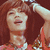 A person with brown hair in a red sleeveless top, winking and raising their right arm, shown in a of four with one blank