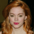 Pixelated close-up of a person with long wavy reddish-brown hair, closed eyes, and pink lips against a dark background.