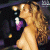 Pixelated image of a woman with long curly hair in profile, wearing dark clothing and purple accents against a green background with pixelated text.