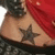 A person's torso with a star tattoo, red fabric draped over shoulder, and dark patterned clothing visible.