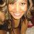 A pixelated close-up of a smiling person with long brown hair wearing a dark top and red accents, set against an indistinct background.