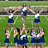 A 4-frame contact sheet of cheerleading poses showing a group performing stunts and individual jumps on a grassy field with bleachers in the background.