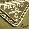 A diamond-shaped Prada logo with 'PRADA MILANO' text, decorative borders, and 'love' script on a textured background.