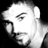 Static grayscale icon of a stylized human face with prominent cheekbones and jawline, featuring a large curved line on the forehead area, rendered in pixelated low-resolution style against black background.