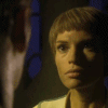 A sequence of showing a person with short brown hair in a dimly lit room, transitioning from standing to lying down with another person