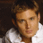 Pixelated close-up of a person with light brown hair wearing a white shirt against dark background.