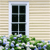 A static pixelated image shows a window with six panes set in a light brown striped wall, with green foliage and blue flowers below.