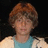 Pixelated image of a person with short brown hair wearing a light blue shirt under a beige jacket against dark background.