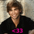 Pixelated image of a person with brown hair wearing a black shirt featuring pink '<33' text against a light background.