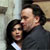 Two people in close physical proximity, one with dark hair wearing a dark jacket over a light shirt, the other with dark hair in a dark jacket, against a blurred background.