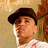Pixelated image of a person with dark hair wearing a white shirt, set against a light brown background.