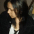 A person with long dark hair wearing a black jacket over white clothing appears in two showing slight head movement