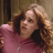 Pixelated image of a person with light brown curly hair wearing a pink top against a blurred background.