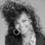 Black-and-white pixelated image of a person with curly hair wearing a large hoop earring and dark clothing against a light background.