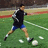 Pixelated image of a person in athletic wear kicking a soccer ball on a grassy field with stadium seating.