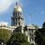Pixelated image of a domed building with columns, flagpole, and trees under a blue sky.