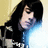 Pixelated image of a person with long dark hair wearing a black jacket over a blue shirt against a light yellow background.