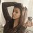 A pixelated image shows a person with long dark hair wearing a black top, holding up a white rectangular object in one hand and a small dark device in the other against a light background.