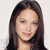 Pixelated portrait of a person with long dark hair, light skin, and pink cheeks against a light gray background.