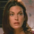 A pixelated close-up of a person with long dark hair, light skin, and brown eyes, wearing a red top against a blurred background.