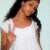 A person in a white top with long dark hair makes a peace sign against a light blue background.