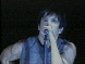 A person singing into a microphone with dark hair and sleeveless top, shown in two against black background