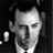 Static grayscale buddy icon of a person's face with dark hair and light clothing, rendered in low-resolution pixel art style against black background.