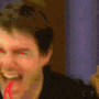 A man in a black shirt interacts with another person on a beige couch, emitting blue electrical effects from his hands while red tongue-like shapes extend from the first person's mouth.