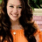 A pixelated image of a person with long brown hair wearing an orange top, positioned on a bright blue background with text elements.