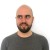 Pixelated static image of a person with a bald head, brown eyes, and a brown beard wearing a dark gray shirt against a white background.