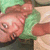A person in a green shirt lies on a light-colored surface with a neutral expression, viewed from above.