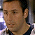 A pixelated close-up of a person's face with short dark hair, wearing a dark shirt, against a blurred background with light and dark tones.