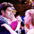 Pixelated image of two figures in a close embrace, one with light hair and pink clothing holding a bright magenta object against a dark background.