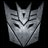 Static grayscale pixelated icon of a Transformer robot face with angular features and V-shaped mouth, set against black background.