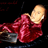 Pixelated figure in red garment reclines on dark background with partial gray object visible.