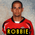 A person in a red sports jersey with black trim stands against a textured background, with yellow text overlays changing across four