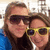 Two people in close proximity, one wearing dark sunglasses and blue clothing, the other in yellow-framed sunglasses and dark clothing, both with brown hair, against a light background with pixelated details.