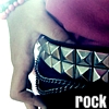 A close-up of a person's torso wearing a black studded belt with silver triangular studs and a purple garment, with the word 'ROCK' in white text at the bottom right.