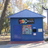 Blue structure with rectangular panels and small square elements against a blurred background of trees and light.