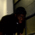 Pixelated static image of a person in dark clothing leaning against a wall with a light-colored vertical element on the left.