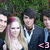 A pixelated group photo of four people outdoors with green foliage background, one person in white dress and pink hair accessory, another in dark suit with light blue shirt.
