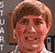 Pixelated static image of a person with light brown hair and fair skin, wearing a white shirt against a dark background.