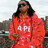 A person in a red hoodie with white text stands against a blurred background of buildings and sky.